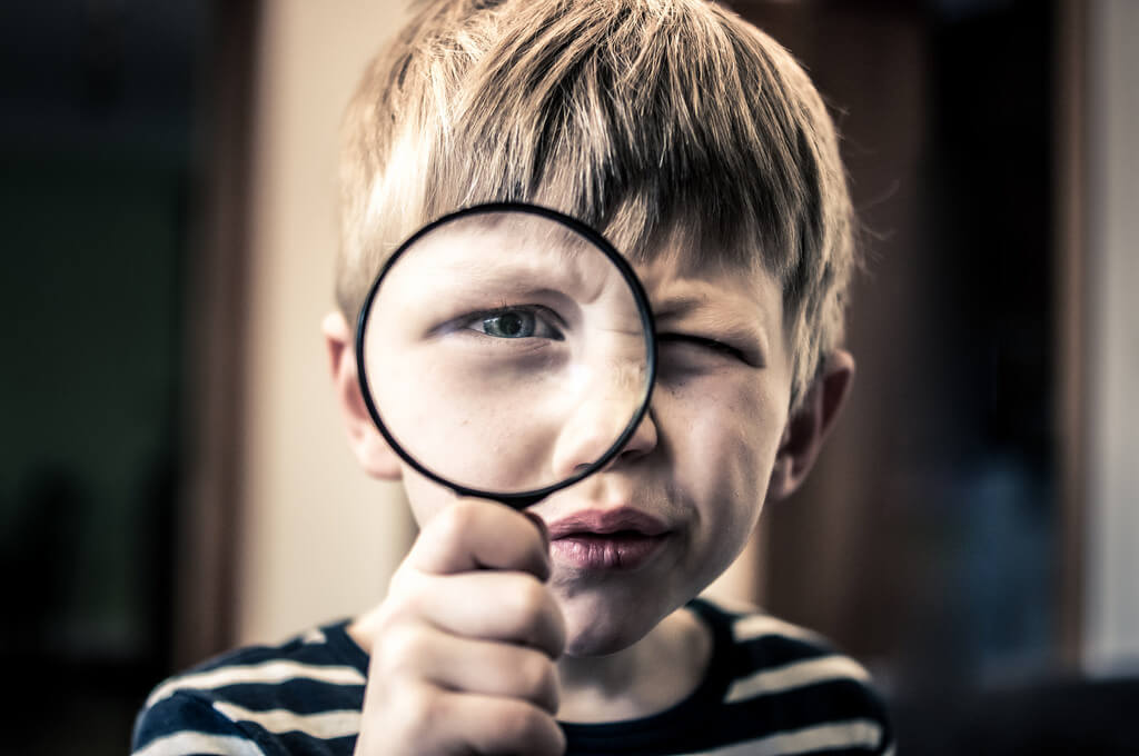 young boy with a magnifying glass, looking at you