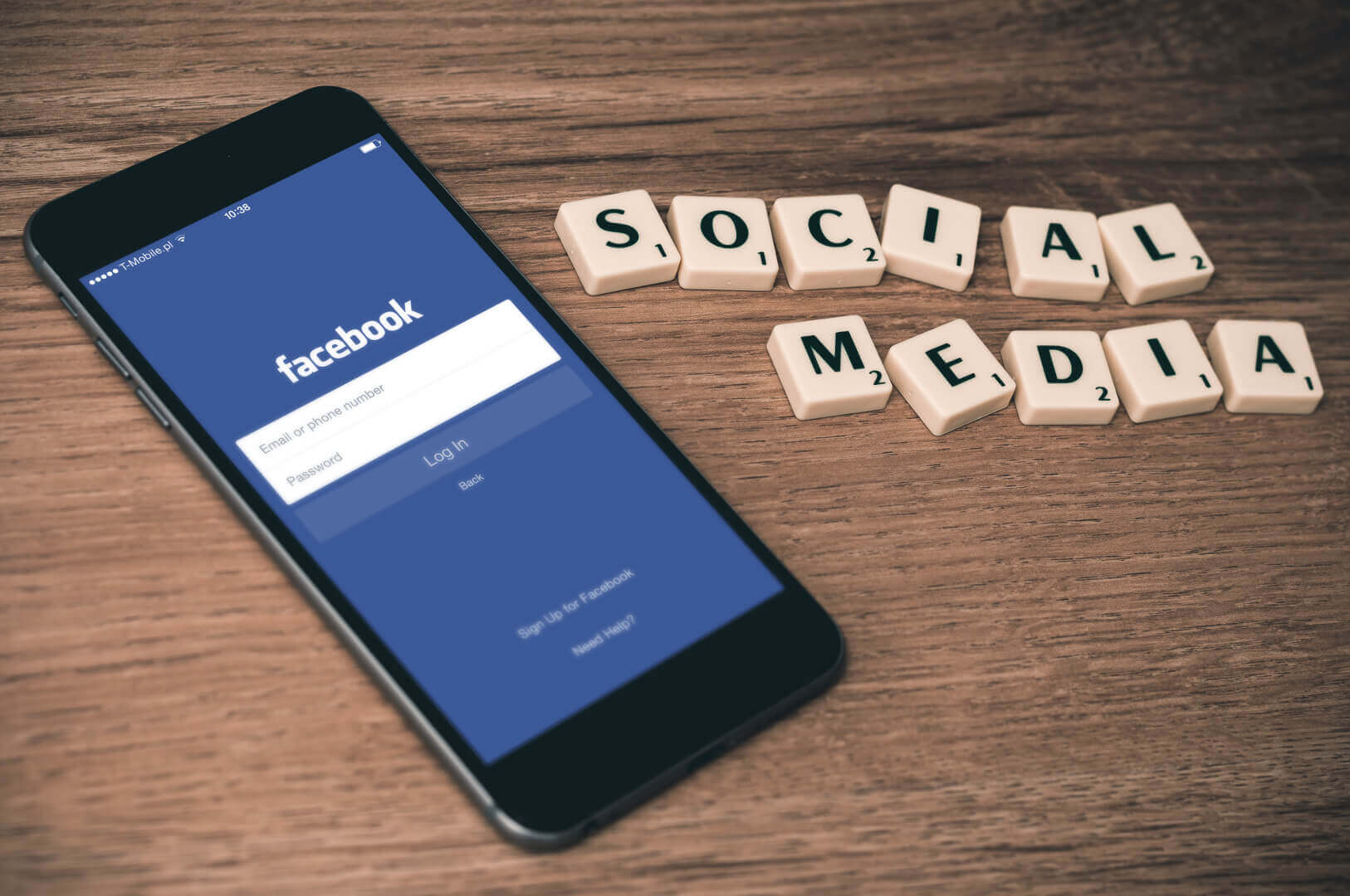 a picture of a smartphone with a Facebook login and lying on the table nearby are some word tiles spelling out "Social Media"